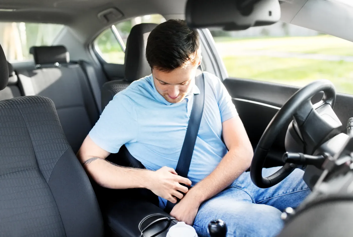 Driver fastening a seat belt inside a vehicle cabin with the steering wheel and windscreen visible