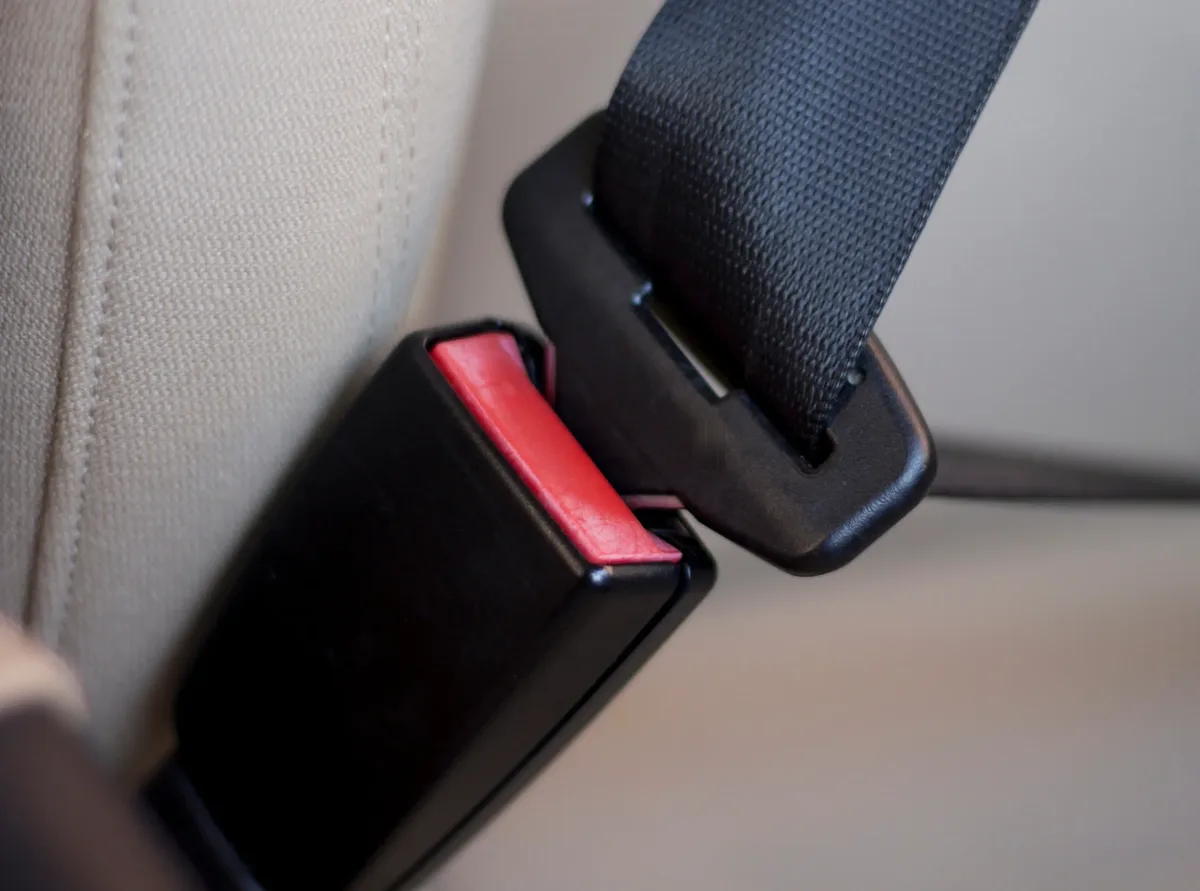 Seat belt buckle with red press release button positioned beside its mating tongue plate