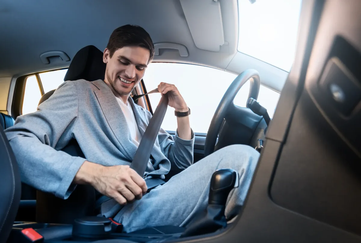 Person seated in the driver seat of a passenger car drawing the seat belt webbing across the body