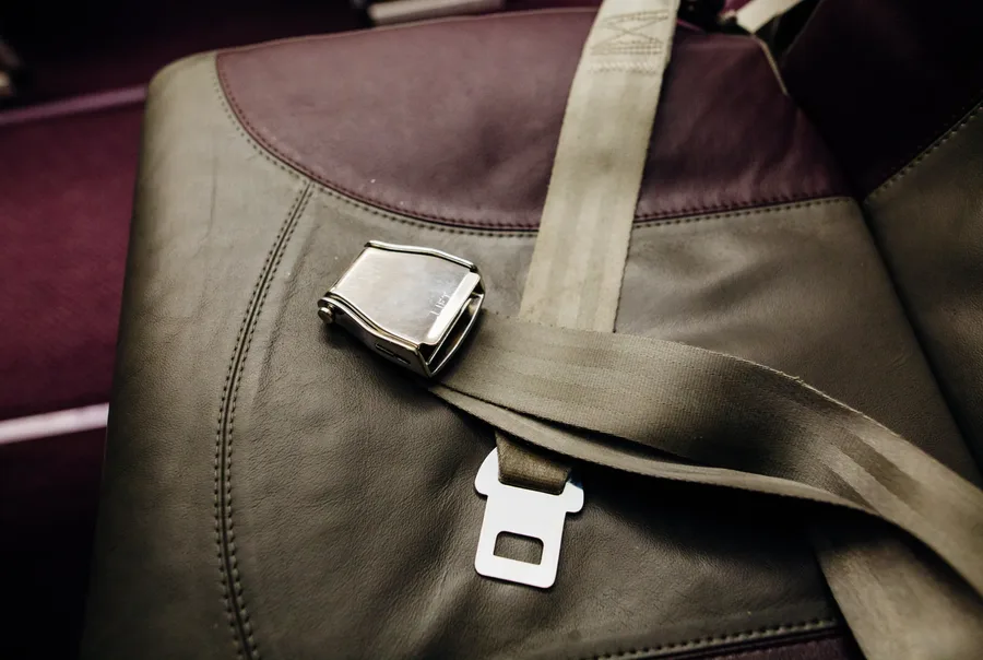 Lift-latch style restraint buckle and webbing fitted to an upholstered transport seat