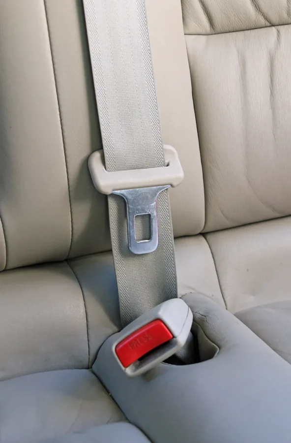 Light coloured seat belt webbing, tongue plate and buckle fitted to a cream leather vehicle seat