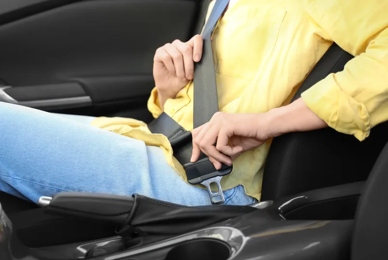 Occupant in a vehicle seat guiding the seat belt tongue plate towards the buckle
