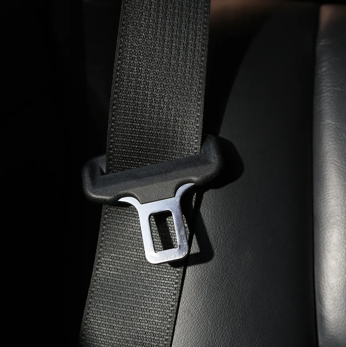 Close view of woven seat belt webbing and a metal tongue plate against a dark leather surface