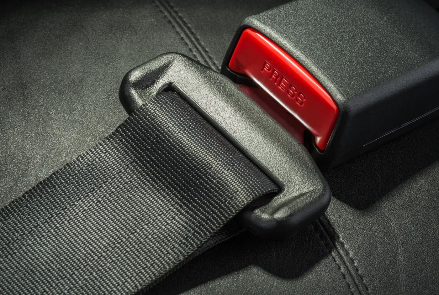 Seat belt webbing feeding through a moulded guide into a buckle assembly with a red release button