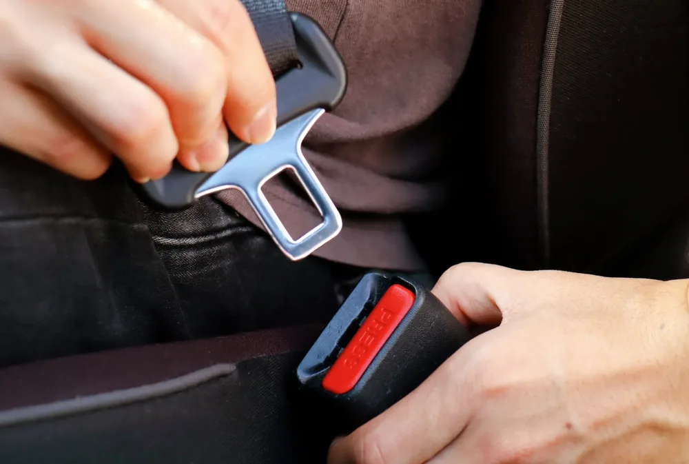 Hands guiding a seat belt tongue plate into a buckle