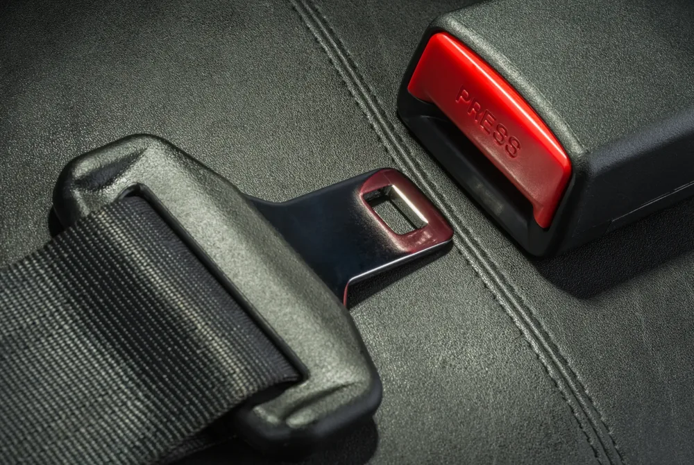 Seat belt assembly with webbing, tongue plate and red release buckle on a dark seat